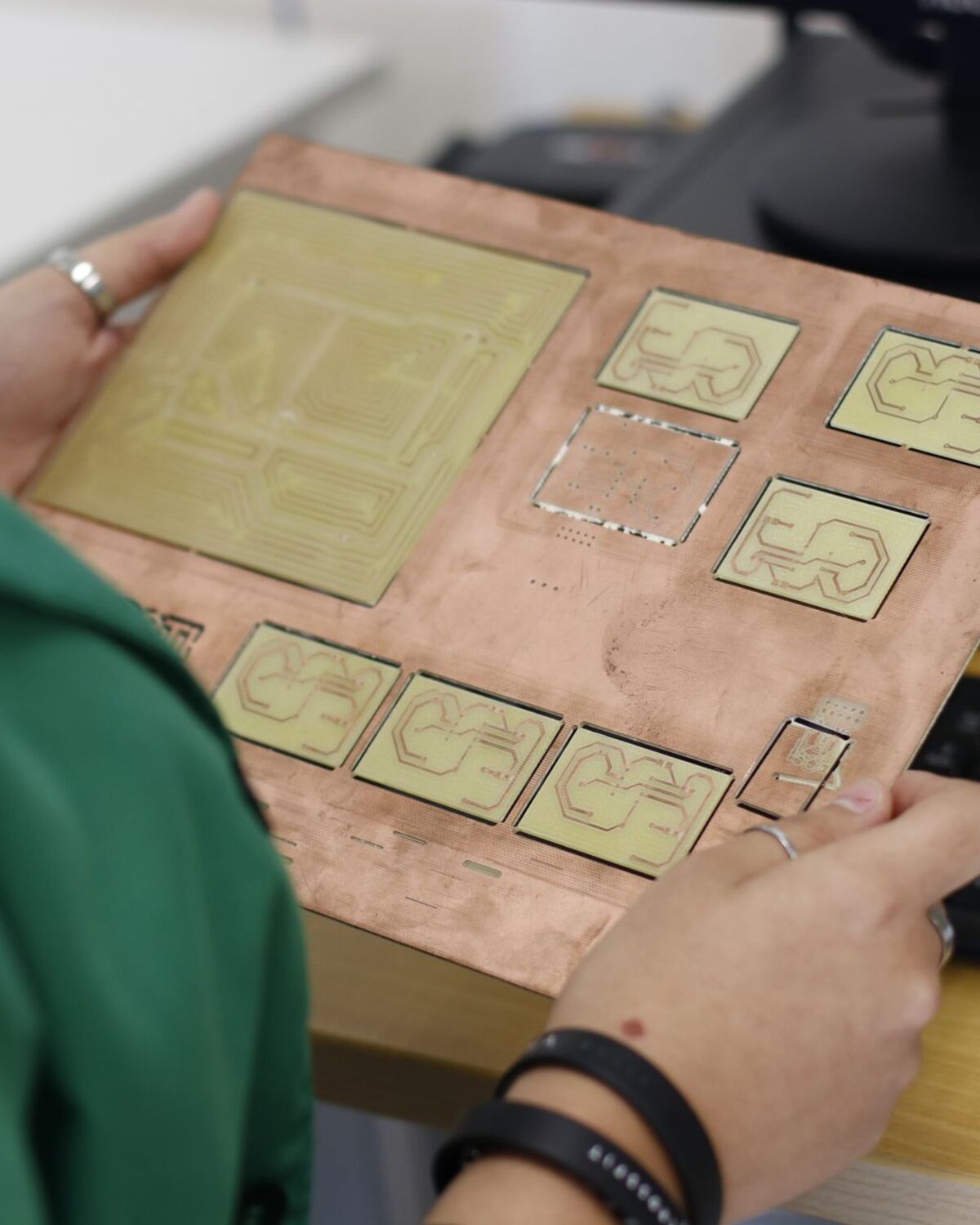 Technician holding a copper-clad panel of milled prototype circuit boards at an engineering workstation.